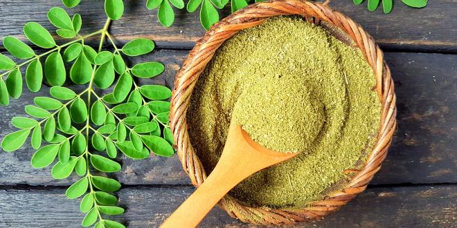a bowl of moringa powder and fresh leaves